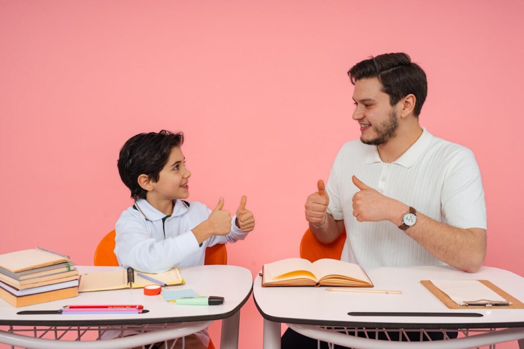 Teacher and student exchanging thumbs up at desk in a learning environment.